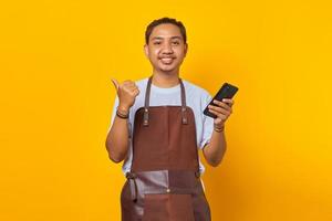 Portrait of cheerful positive man holding smartphone with finger showing sales discount over yellow background photo