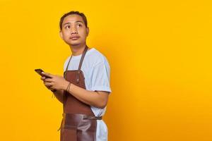 Portrait of happy young Asian man using smartphone and looking at empty space on yellow background photo