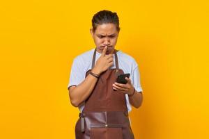 Young Asian man holding smartphone looks anxious and worried afraid of something isolated over yellow background photo