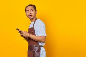 Portrait of surprised Asian young man using smartphone and looking aside on yellow background photo