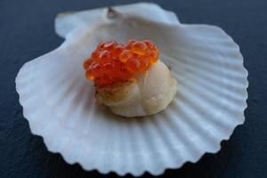 Scallop on a shell with a cap of red caviar. photo