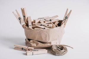 Wooden clothespins in paper bag with rope on white background. Place for your text photo