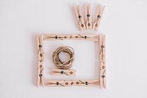 Wooden clothespins with rope on white background which are composed in the form of a photo camera icon. View from above. Place for your text