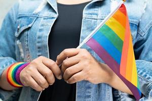 Asian lady wearing blue jean jacket or denim shirt and holding rainbow color flag, symbol of LGBT pride month celebrate annual in June social of gay, lesbian, bisexual, transgender, human rights. photo