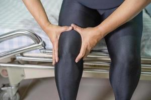 El paciente asiático de la mujer de la señora de mediana edad toca y siente el dolor de su rodilla, concepto médico sano. foto