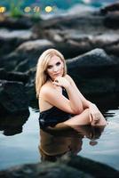 blonde girl in a black dress with blue eyes on the coast of the river photo