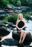 blonde girl in a black dress with blue eyes on the coast of the river photo