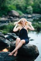 blonde girl in a black dress with blue eyes on the coast of the river photo