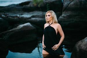 blonde girl in a black dress with blue eyes on the coast of the river photo