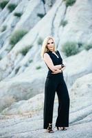 blonde girl in a black trouser suit with blue eyes on the background of a granite quarry photo