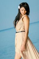 girl with black hair in a beige dress on the shore of the ocean photo