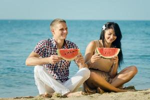 guy and a girl on the seashore eating a ripe watermelon photo