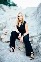 blonde girl in a black trouser suit with blue eyes on the background of a granite quarry photo