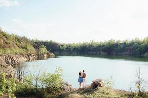 una pareja joven, un chico y una chica caminan cerca de un lago de montaña rodeado foto