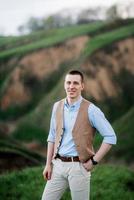 a young guy in a brown suit on the background of mountain green slopes photo