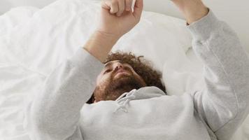 homem deitado na cama segurando um smartphone enquanto move a cabeça e cantarola