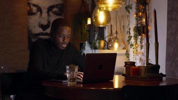 Hombre sentado a la mesa mirando y escribiendo en un teléfono inteligente y una computadora portátil