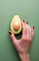 Half an avocado in a hand on the green background top view
