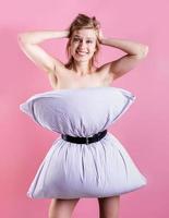 young beautiful woman dressed in pillow laughing isolated on pink background photo