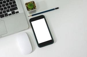 Top view mock up smart phone white blank screen and pencil mouse computer laptop flat lay on desk. photo