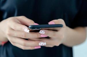 mano femenina sosteniendo un teléfono con un hermoso esmalte de uñas rosa foto