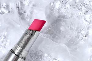 Lápiz labial rojo rosa en tubo plateado sobre fondo de hielo, espacio de copia foto