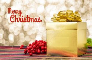 Merry Christmas word with Gold present box and ribbon on table with sparkling gold bokeh photo