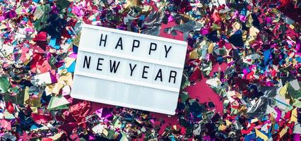 Caja de luz de feliz año nuevo sobre fondo de confeti de colores foto