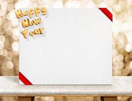 Feliz año nuevo representación 3d de oro y tarjeta blanca con cinta roja en la habitación de perspectiva con una pared de bokeh brillante en una mesa de mármol foto