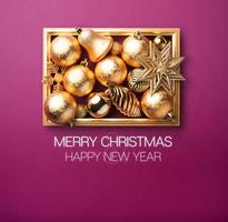 Feliz navidad y próspero año nuevo bola de decoración navideña de oro brillante y estrella con marco dorado en púrpura foto