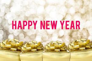 Feliz año nuevo palabra con caja de regalo dorada con cinta y confeti de colores en desenfoque boekh de copo de nieve dorado