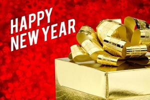 Feliz año nuevo palabra con caja de regalo dorada con cinta y confeti de colores en rojo borroso foto