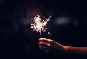 Mano sujetando una explosión de bengala ardiente sobre un fondo negro en la noche, fiesta de celebración navideña foto