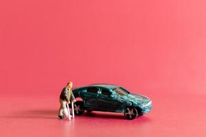 Miniature people broken leg man patient with bandage walking with crutch with toy car wreck photo