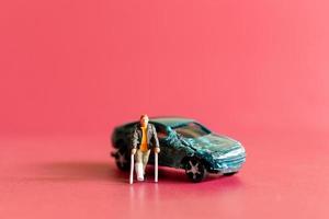 Miniature people broken leg man patient with bandage walking with crutch with toy car wreck photo