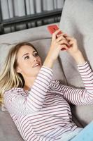 Smiling woman using her smartphone lying on the sofa. photo