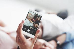 Focused photo of the phone holding by man who taking selfie with friends that laying down