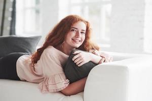 Photo of the young girl laying down on the white sofa and smiling