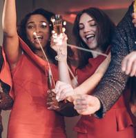 Hands up and partying. Multiracial friends celebrate new year and holding bengal lights and glasses with drink photo