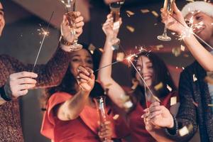 pide un deseo. amigos multirraciales celebran el año nuevo y sostienen luces de bengala y vasos con bebida