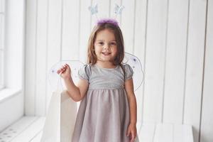 Smiling with paper package in right hand. Close up photo. Beautiful little girl with fairy costume having fun posing for the pictures photo
