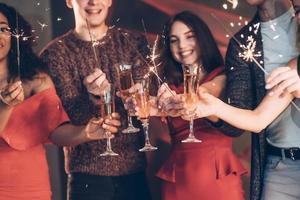 Sparkles everywhere. Multiracial friends celebrate new year and holding bengal lights and glasses with drink photo