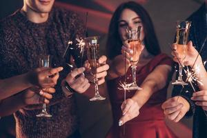 bien vestido. amigos multirraciales celebran el año nuevo y sostienen luces de bengala y vasos con bebida foto