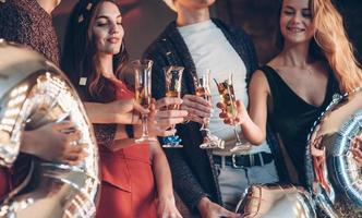 Holding silver balloons. Photo of the company of friends having the party with alcohol