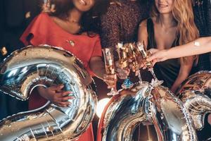 estos confeti incluso en las copas de champán. globos plateados y bebidas. grupo de personas en la fiesta de año nuevo foto