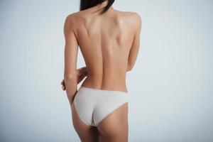 Girl with perfect body in white underwear turning her back to the white background in the studio photo