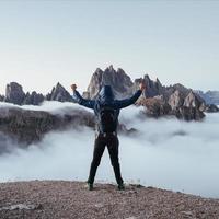Touristic man raised his hands up on the beautiful daylight mountains full of fog