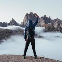 Raising fist up. Touristic man raised his hands up on the beautiful daylight mountains full of fog photo