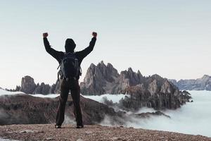 New achievement. Touristic man raised his hands up on the beautiful daylight mountains full of fog photo