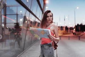 Young female traveler holding the map and searching the place at evening time photo